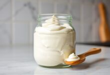 Um pote de vidro com requeijão cremoso homogêneo e brilhante, misturado com creme de leite, pronto para ir ao freezer.