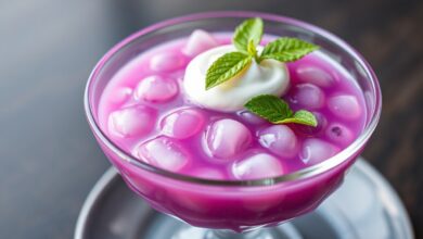 Tigela de sagu de um roxo vibrante e translúcido, servido gelado e decorado com folhas de hortelã.
