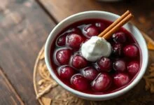 Tigela de sagu de vinho com grãos translúcidos vermelho-escuros, caldo encorpado e brilhante, finalizado com uma colherada de creme de leite branco ao lado