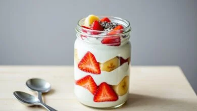 Pote de vidro transparente com camadas alternadas de iogurte branco cremoso e frutas frescas coloridas, finalizado com sementes de chia.