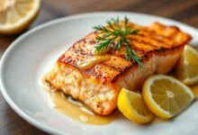 Filé de salmão perfeitamente grelhado, com pele crocante dourada e carne rosada e macia, finalizado com molho cítrico brilhante e fatias de limão fresco.