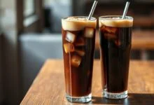 Dois copos altos com a bebida gaseificada, cheios de gelo e espuma, prontos para servir.
