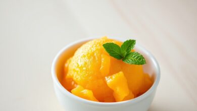 Uma bola vibrante de sorbet de manga laranja em uma tigela branca, com textura cremosa e raspas de limão, perfeita para um dia quente.