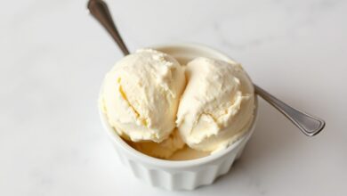 Bola de sorvete caseiro de cor creme uniforme, textura lisa e densa, servida em tigela branca com uma colher de metal, fundo limpo e iluminação natural.