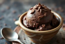 Porção generosa de sorvete de chocolate escuro e aveludado, servido em tigela de cerâmica rústica, com lascas de chocolate e uma colher.