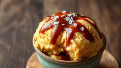Tigela de sorvete de creme com caramelo denso e sedoso, cor caramelo âmbar, coberto por um fio de calda escura e floco de flor de sal, servido em fundo rústico de madeira.