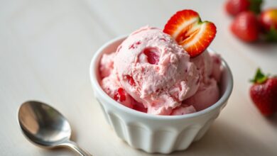 Tigela de sorvete cremoso de morango rosa vibrante com pedaços de fruta e uma colher de sorvete ao lado.