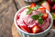 Tigela de sorvete caseiro de morango com cor rosa vibrante e textura aveludada, guarnecido com frutas frescas.