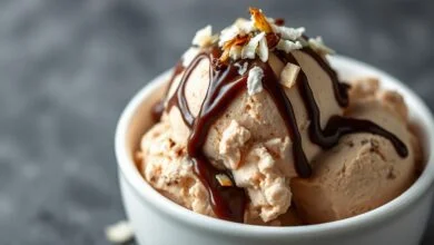 Porção generosa de sorvete prestígio cremoso em tigela de cerâmica, com calda de chocolate e flocos de coco.