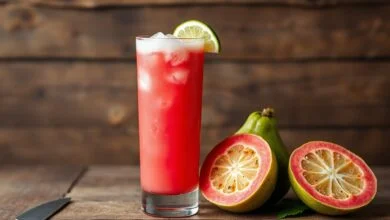 Um copo alto de suco de goiaba vibrante, com espuma natural e pedaços de gelo, servido em fundo de madeira rústica.