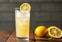 Um copo alto de suco de limão com casca, levemente turvo, com bastante gelo e uma rodela de limão fresco na borda, pronto para ser servido.