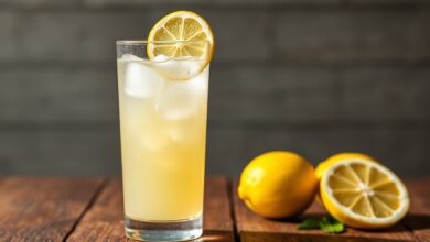 Um copo alto de suco de limão com casca, levemente turvo, com bastante gelo e uma rodela de limão fresco na borda, pronto para ser servido.