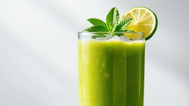 Um copo alto de vidro transparente contendo o suco verde vibrante e homogêneo, decorado com folhas de hortelã fresca e fatias de limão na borda.