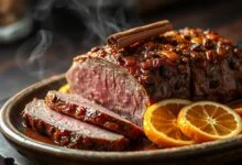 Fatias de tender com laranja e especiarias, com crosta dourada e brilhante, dispostas sobre uma travessa de cerâmica, rodeado por fatias de laranja caramelizado e aromas de canela.