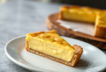 A torta finalizada, com a superfície dourada e rachada levemente no centro, fatiada para revelar o interior aveludado.