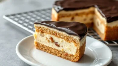 Torta fatiada sobre prato de porcelana, expondo o recheio cremoso e claro com pedaços de castanha, base crocante de biscoito e cobertura de chocolate escuro e brilhante.