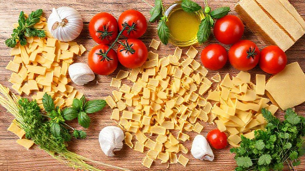 Visão de cima mostrando os ingredientes básicos para preparo de macarrão e molho organizados em uma bancada.
