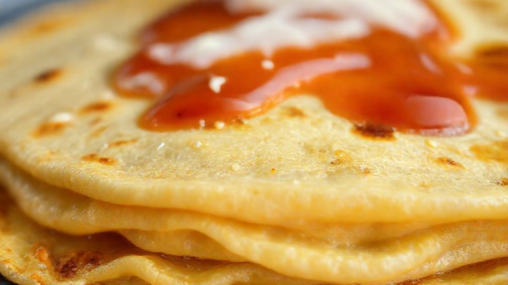 Close-up da panqueca douradinha, mostrando a textura fina e o recheio cremoso no corte.